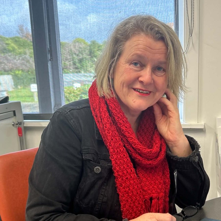 Alison smiling at her desk, wearing a red scarf